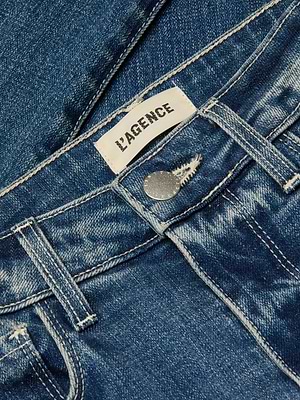 Close-up of the Ruth Straight-Leg Jean in indigo denim, featuring the waistband, belt loops, a silver button, and a white L’AGENCE brand label stitched inside.