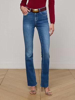 A person wearing a red long-sleeve top, L'AGENCE Ruth Straight-Leg Jeans with a brown belt, and beige heeled sandals stands on a wooden floor against a plain light wall.