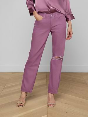 A person wears Nevia Slouchy Straight-Leg Jeans in faded purple with a ripped knee, a matching satin shirt, and beige sandals, standing on a light wooden floor against a plain gray wall. Their face is not visible.