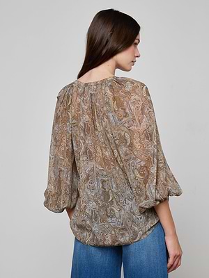 A woman with long brown hair, seen from the back, wears the Teagan Blouse—a semi-sheer paisley print crinkle poly chiffon top with three-quarter sleeves—paired with blue jeans against a plain light gray background.