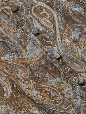 Close-up of the Teagan Blouse in brown paisley print with intricate blue and tan details, crafted from crinkle poly chiffon and featuring round fabric-covered buttons on its semi-sheer surface.