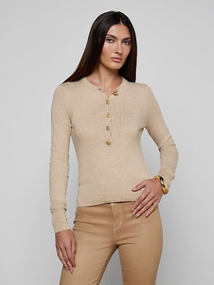 A woman with long, straight dark hair models the Ronda Knit Henley Top in beige with gold buttons and tan pants. She poses against a plain light background, one hand on her hip and the other by her side.
